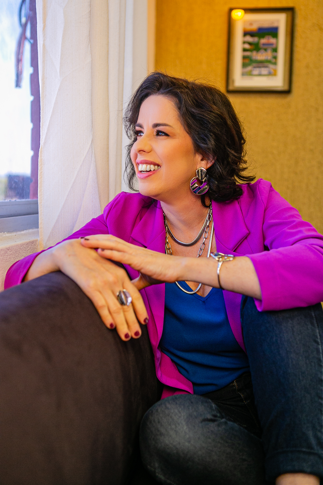 Carol Nogueira sorrindo, em sessão de fotos com blazer magenta